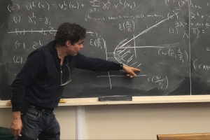 Geanakoplos pointing to an equation on the blackboard